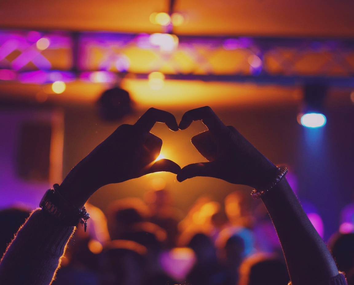 Public d'un concert formant un cœur avec les mains